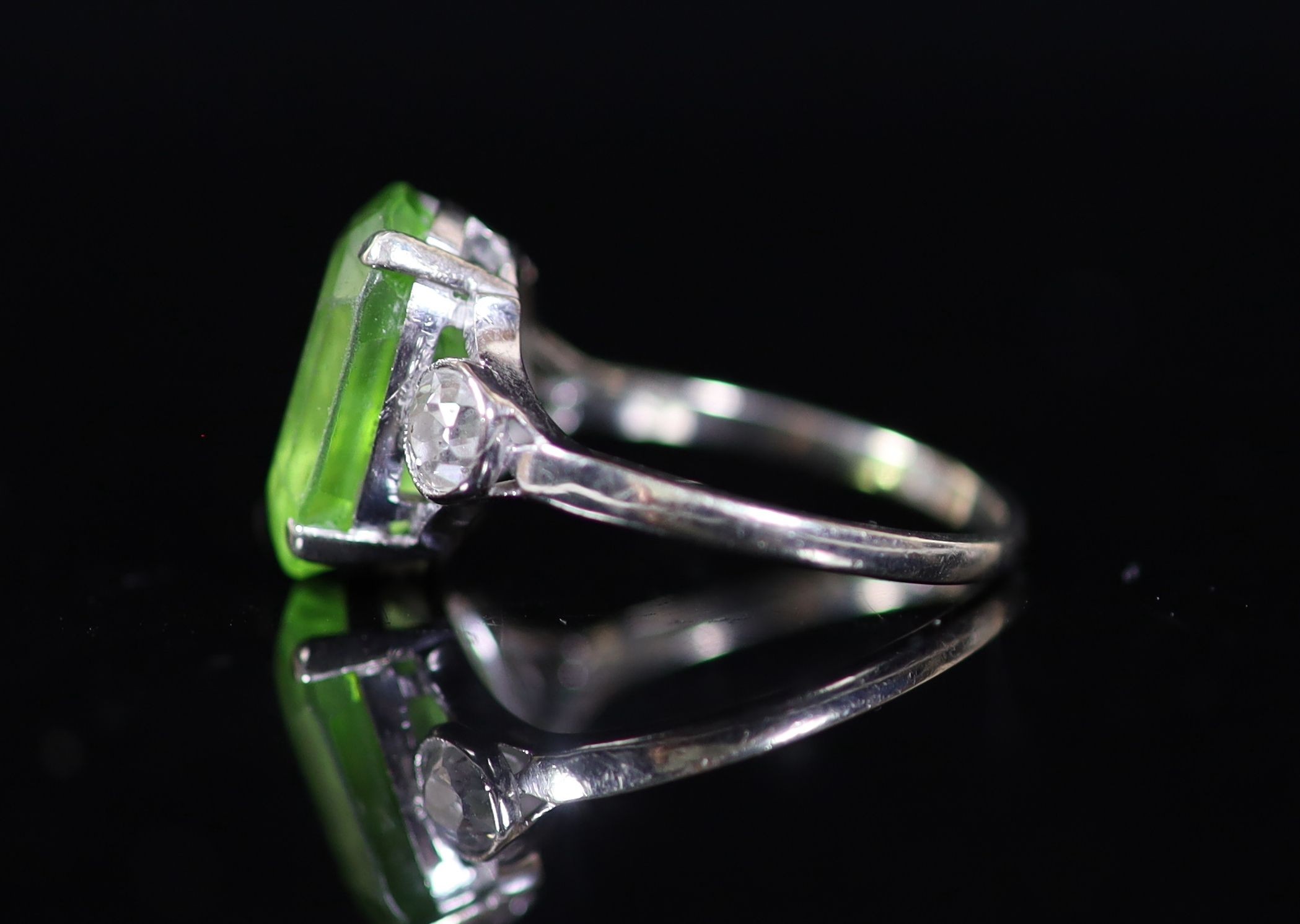 A 9ct white gold oval cut peridot set dress ring, with diamond set shoulders